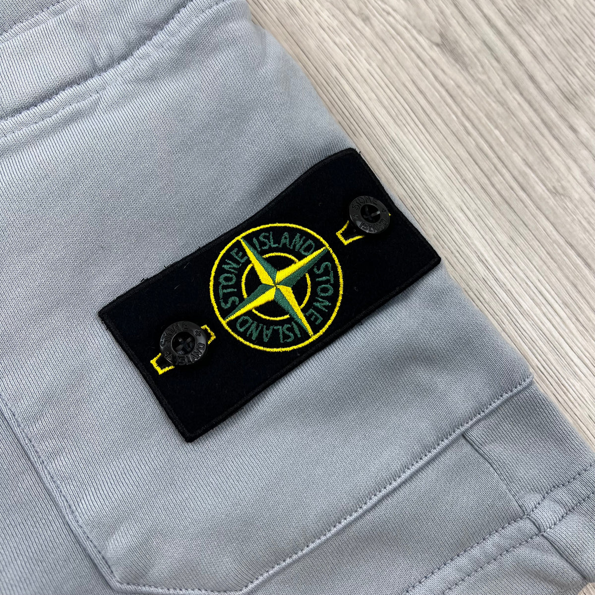A close up view of the compass badge on the Stone Island Jersey Shorts in Ash Grey.