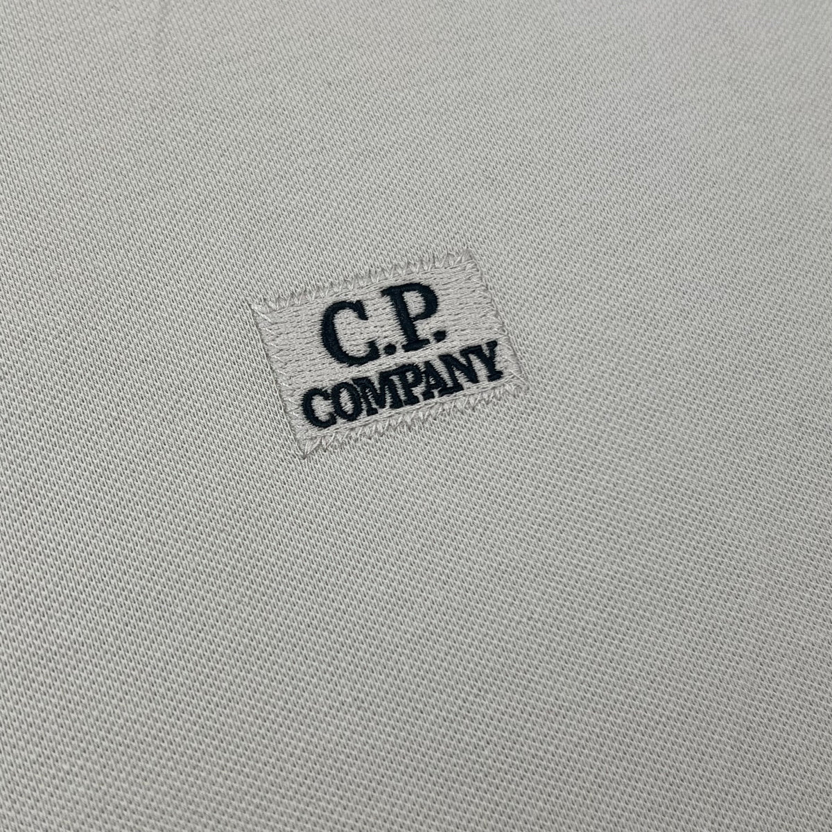 Close up view of the embroidered logo patch on a CP Company Stretch Piquet Polo Shirt in Silver Birch.
