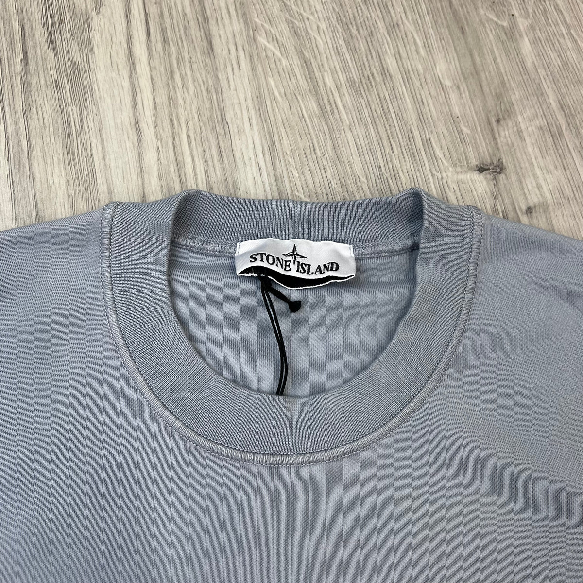 A close up view of the crewneck and label on a Stone Island Crewneck Sweatshirt in Ash Grey.