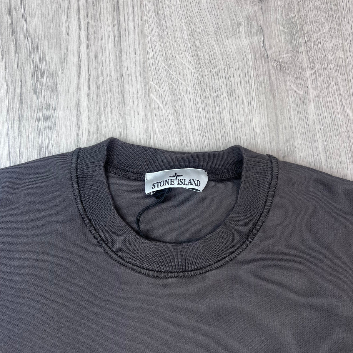 A close up view of the crewneck and label on a Stone Island Crewneck Sweatshirt in Charcoal Grey.