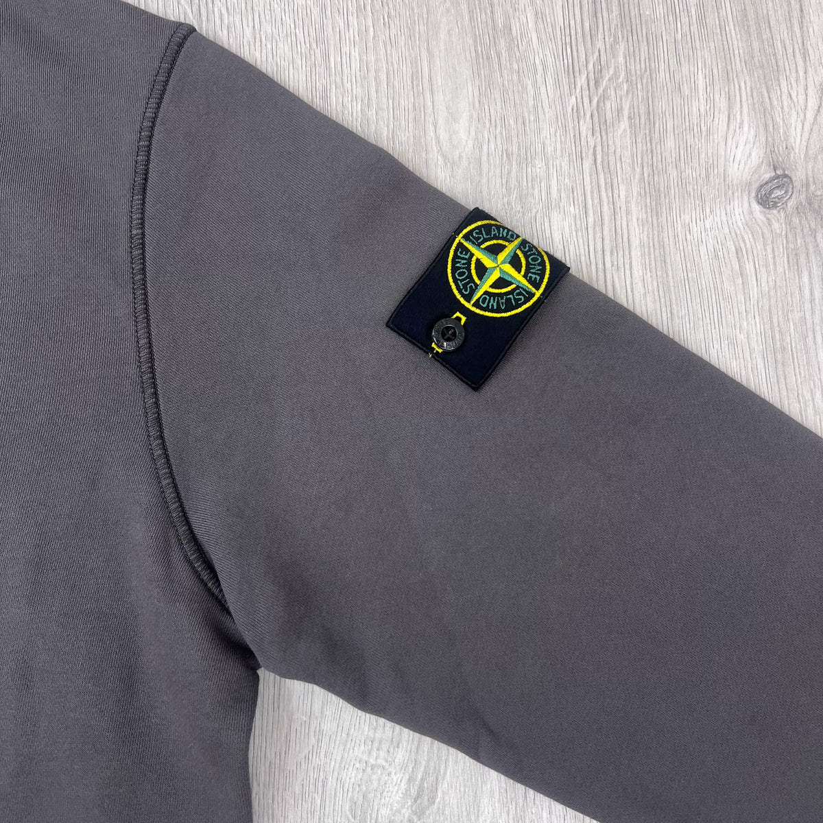 A close up view of the compass badge on a Stone Island Crewneck Sweatshirt in Laurel Green.