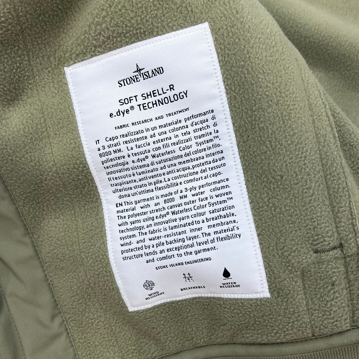 A close up view of the engineering label on the inside of a Stone Island Soft Shell-R_e.dye® Jacket in Laurel Green.